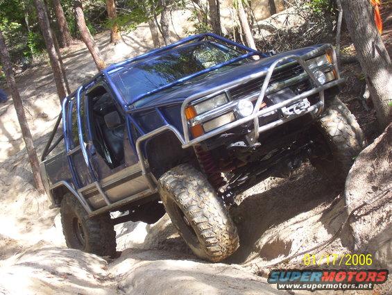 Blue off-road vehicle with roll cage and brush guard climbing over rocks