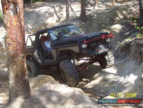 Black off-road SUV with large tires navigating a dirt trail, red winch bar on front