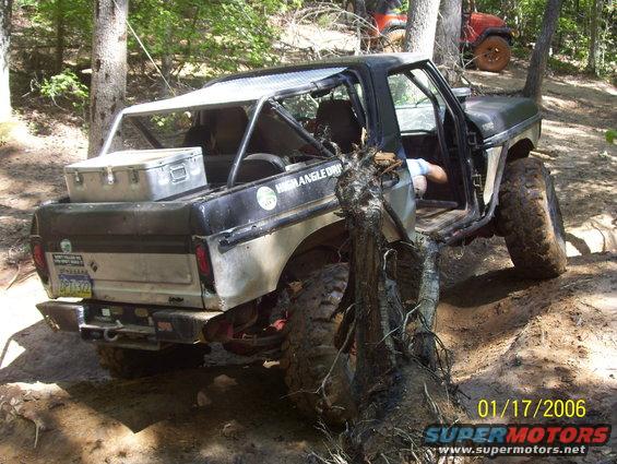 1978 Ford Bronco off-road with door open, stuck on a tree. Another vehicle is visible in the background
