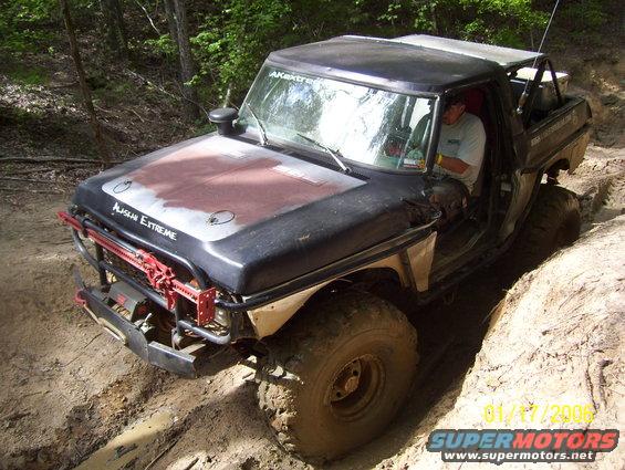 Modified pickup truck with off-road tires and roll cage navigating a dirt trail. Text on hood reads 'ALASKAN EXTREME'