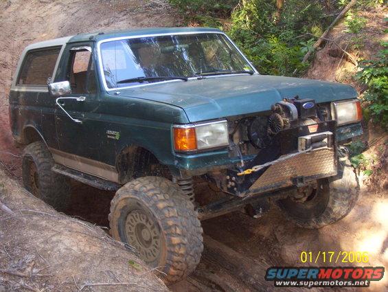 Green Ford Bronco with a white top, lifted suspension, and off-road tires navigating a dirt trail