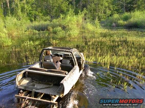 off-road vehicle driving through shallow water and tall grass