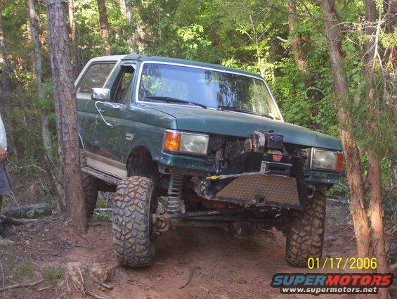 Green Ford Bronco with large tires and winch, angled on a dirt trail