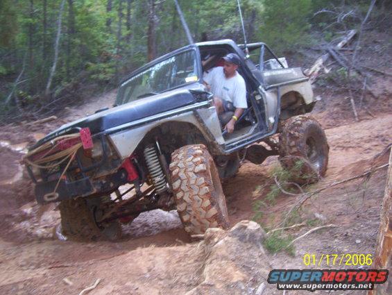 1978 Ford Bronco on muddy trail, driver visible, lifted suspension, off-road tires