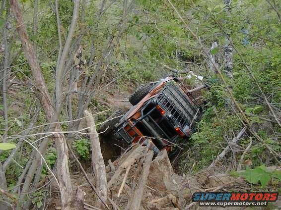 Orange 1988 Ford Bronco tipped on its side in a wooded area
