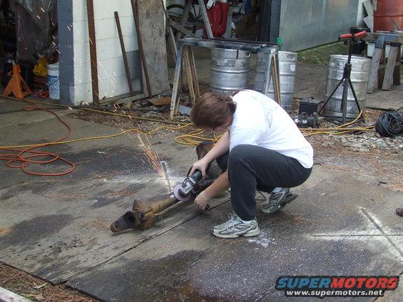 Person crouched down, using an angle grinder on a metal axle with sparks flying