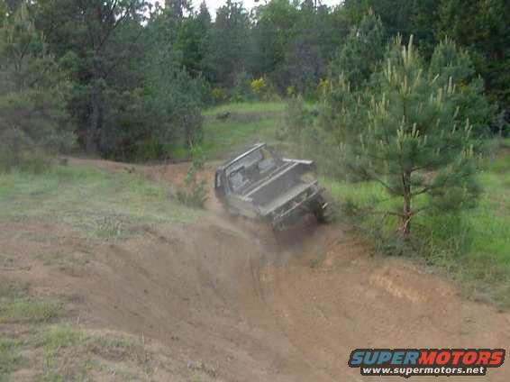 Gray pickup truck driving off-road on a dirt hill, kicking up dust