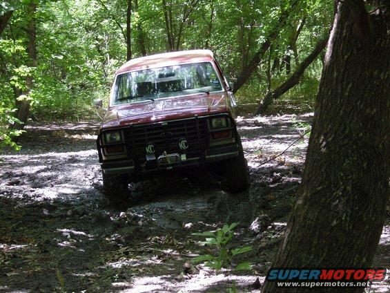Red SUV stuck in a muddy wooded area. It has KC lights on the front