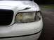2000 Ford Crown Victoria - The front end of a white 2000 Ford Crown Victoria shows significant damage to the headlight and hood.