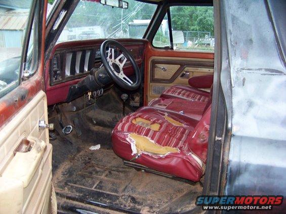 Interior of a 1978 Ford Bronco with torn red striped seats, aftermarket steering wheel, and dirty floor