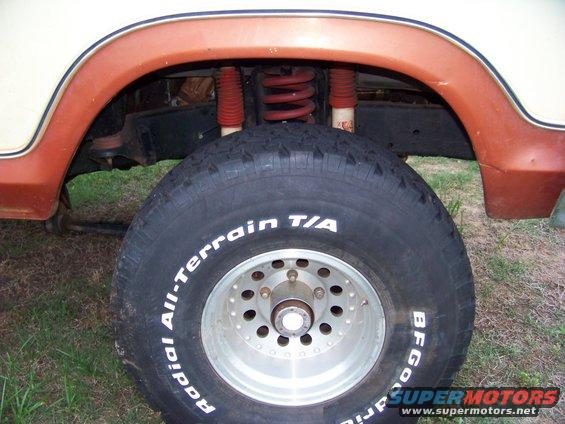 Close-up of a 1979 Ford Bronco's front wheel and suspension system, showing the BFGoodrich All-Terrain T/A tire and orange fender flare
