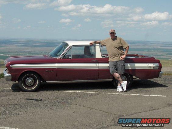 1965 Ford Ranchero with a man standing next to it, parked outdoors with a scenic background