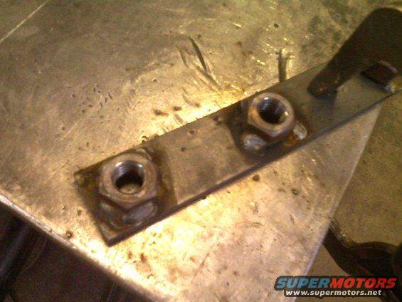 Metal bracket with two welded nuts on a workbench