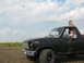 1985 Ford Bronco - A black Ford Bronco with two people inside is parked in a field of sunflowers under a cloudy sky.