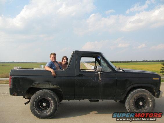 Black Ford Bronco with two people in the cab and bed, side view