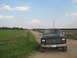 1985 Ford Bronco - A black Ford F-Series truck is parked on a dirt road with a field to the left and farmland to the right under a cloudy sky.