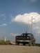 1985 Ford Bronco - A black pickup truck with two people inside drives down a dirt road under a cloudy sky.