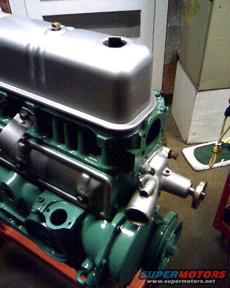 Close-up of a green engine block with a silver valve cover and some attached metal components