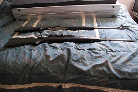 Two rifles laid out on a bedspread. One has a scope