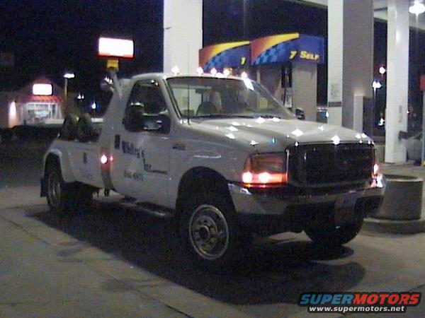 White tow truck with 'Walling & Sons' text on door, parked at gas station at night