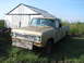 1971 International Travelall - A gold 1971 International Travelall pickup truck sits in front of a weathered barn, its wooden bumper a makeshift addition.