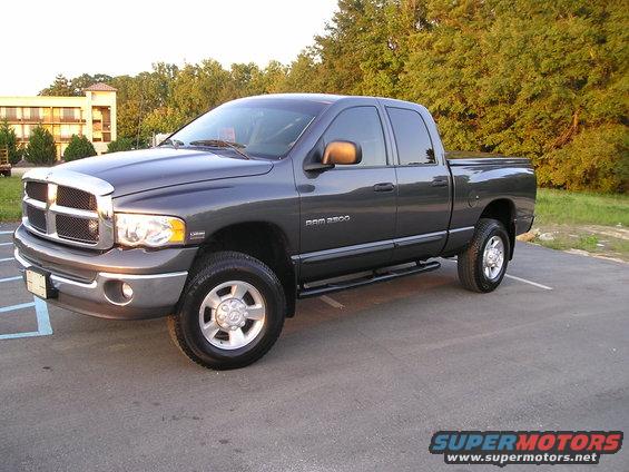 Dark gray Dodge Ram 2500 pickup truck, 3/4 front view, parked on asphalt with trees and a building in the background