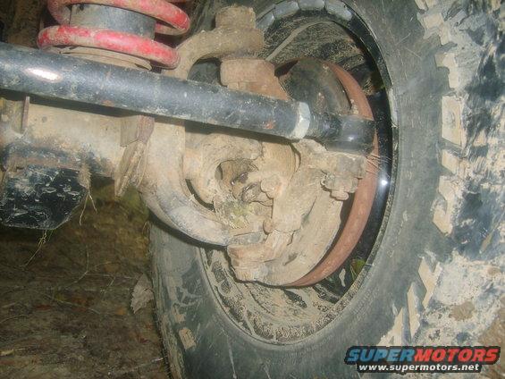 Close-up of a vehicle's front suspension and tire with a Supermotors.net watermark