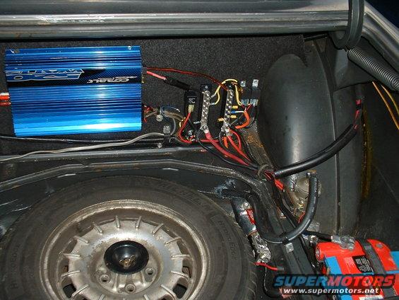 Car trunk interior with spare tire, blue audio amplifier, and wiring