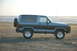 1984 Ford Bronco II - A two-tone blue and grey 1984 Ford Bronco II is seen from the side on a sandy beach with the ocean in the background.