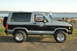 1984 Ford Bronco II - A 1984 Ford Bronco II is seen from the side, parked near the water with a person in the background.