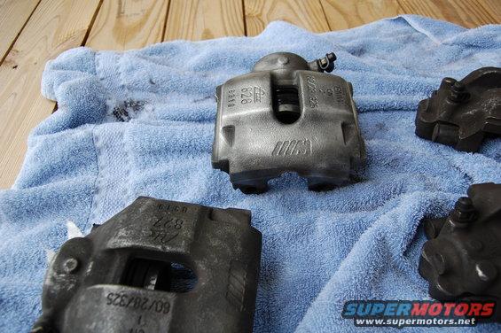 Three BMW M brake calipers on a blue towel. One caliper has "M" logo and "BMW" text
