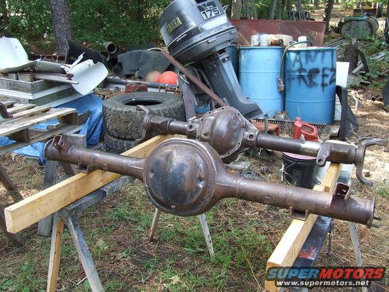 Two rusty rear axles are on sawhorses outdoors. A Yamaha outboard motor is behind them