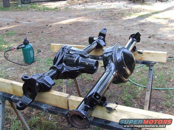 Two black differential axles on sawhorses, one with a green spray bottle nearby