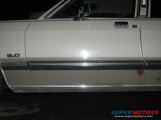 Side view of a beige car with a '5.0' badge and rust on the lower body trim