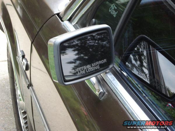 Side view of a dark brown car showing the side mirror with a reflection and a 'Ford' logo on the window