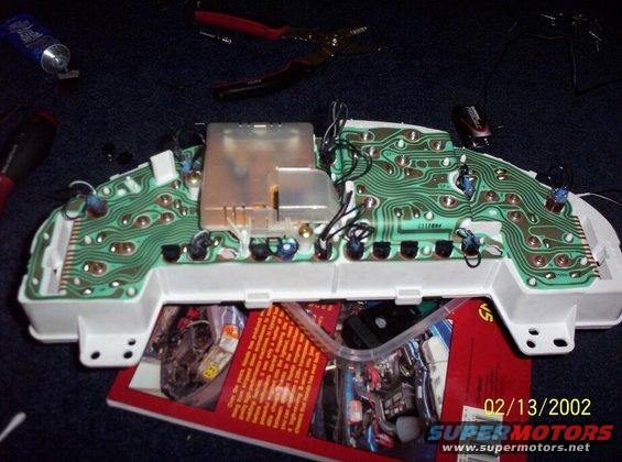 Back of a car instrument cluster circuit board with wiring and components, on top of a red car engine magazine.
