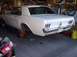 1967 Ford Mustang - A white 1967 Ford Mustang coupe is shown from the rear while undergoing maintenance in a garage.