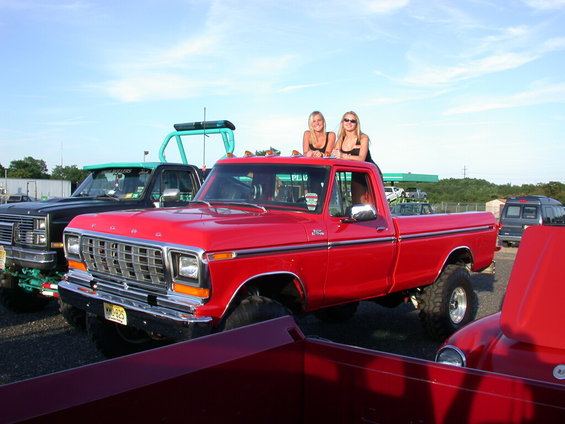 Red 1979 Ford F-250 pickup truck with lifted suspension and two women on the roof