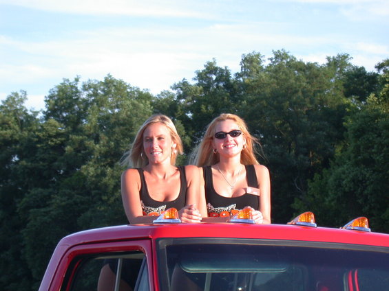 Two women stand on the roof of a red truck with amber lights on top