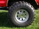 1979 Ford F-250 - This image shows a close-up of a red truck's tire and chrome rim, with 'SUPER SWAMPER RADIAL' visible on the tire.