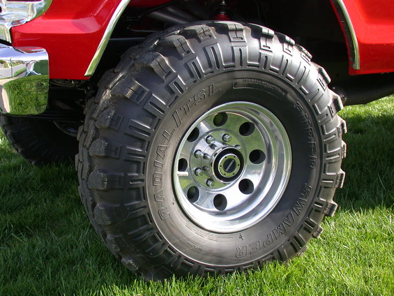 Red vehicle fender and large off-road tire with chrome rim on grass