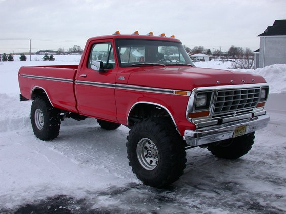 Red 1979 Ford F-250 pickup truck with large tires parked in snow