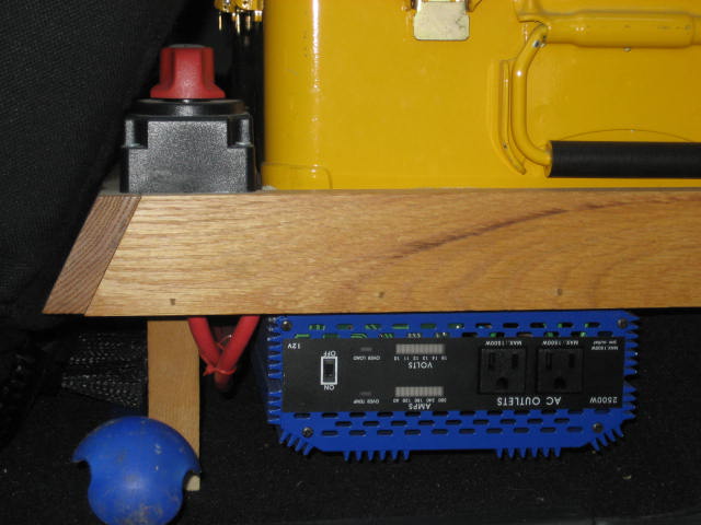 Blue power inverter with AC outlets and a red-knobbed battery disconnect switch mounted on wood