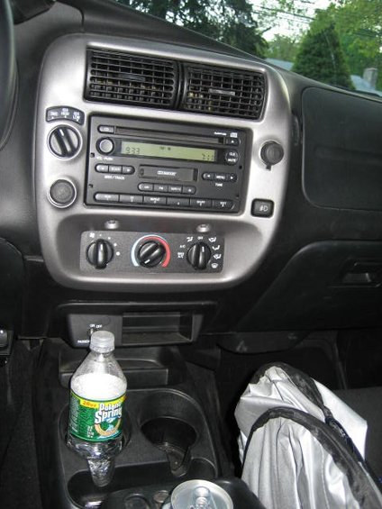Interior of a 2004 Ford Ranger showing the center console with radio, climate controls, cup holders, and a bottle of water