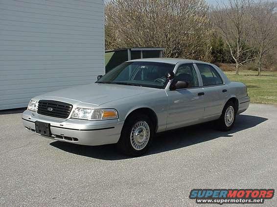 Silver 2000 Ford Crown Victoria sedan, front 3/4 view, parked on asphalt in front of a light-colored building