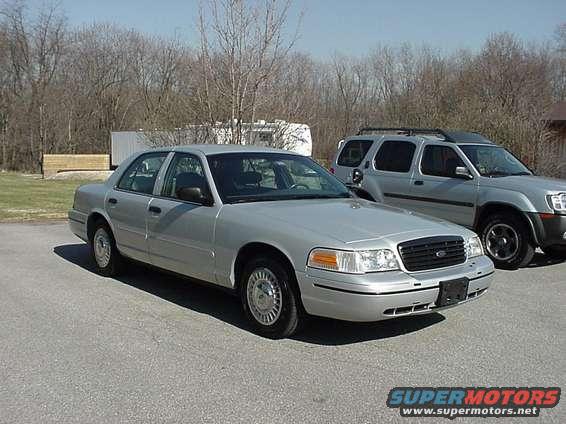 Silver 2000 Ford Crown Victoria sedan, 3q front view, parked next to an SUV
