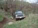 1984 Ford Bronco II - A black SUV navigates a grassy, wooded trail with a rocky embankment.