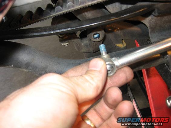 Hand holding a metal rod with a ball joint end near a motorcycle's belt drive system