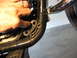 2004 Harley-Davidson Sportster Custom - Close-up of a motorcycle's frame with a hand indicating a mounting bracket. The Supermotors.net logo is visible.