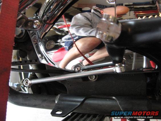 Motorcycle frame with chrome accents and visible engine parts. A person is reflected in the chrome